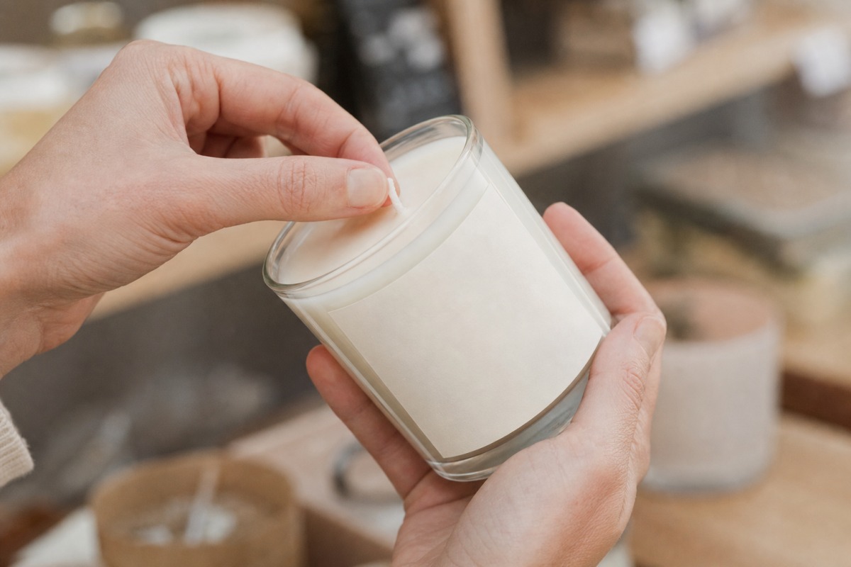 Des mains examinent la mèche en coton et l'étiquette vierge d'une bougie avant l'achat dans un magasin