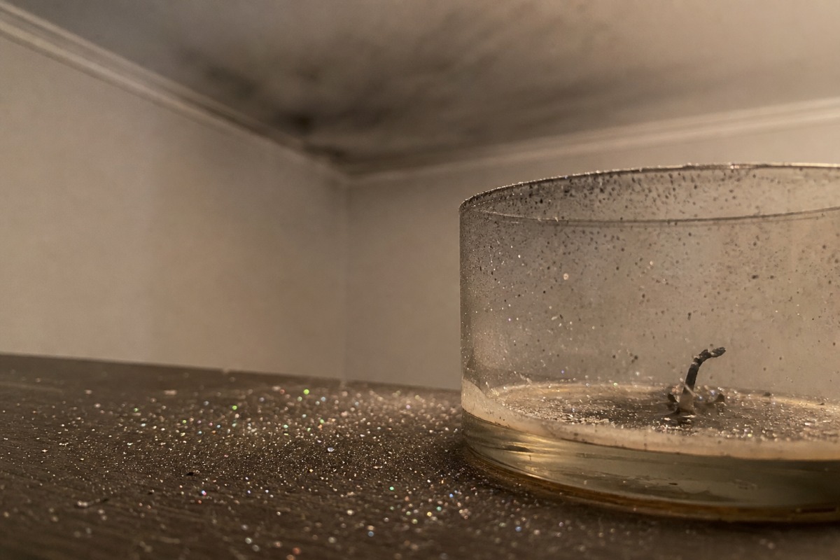 De fines paillettes éparpillées sur la table autour d'une bougie consumée, avec en arrière-plan un mince film gris de suie au plafond.